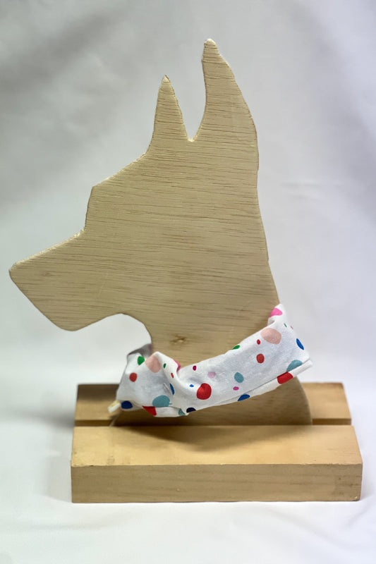 Polka dot pet collar cover on a wooden dog-shaped stand against a white background